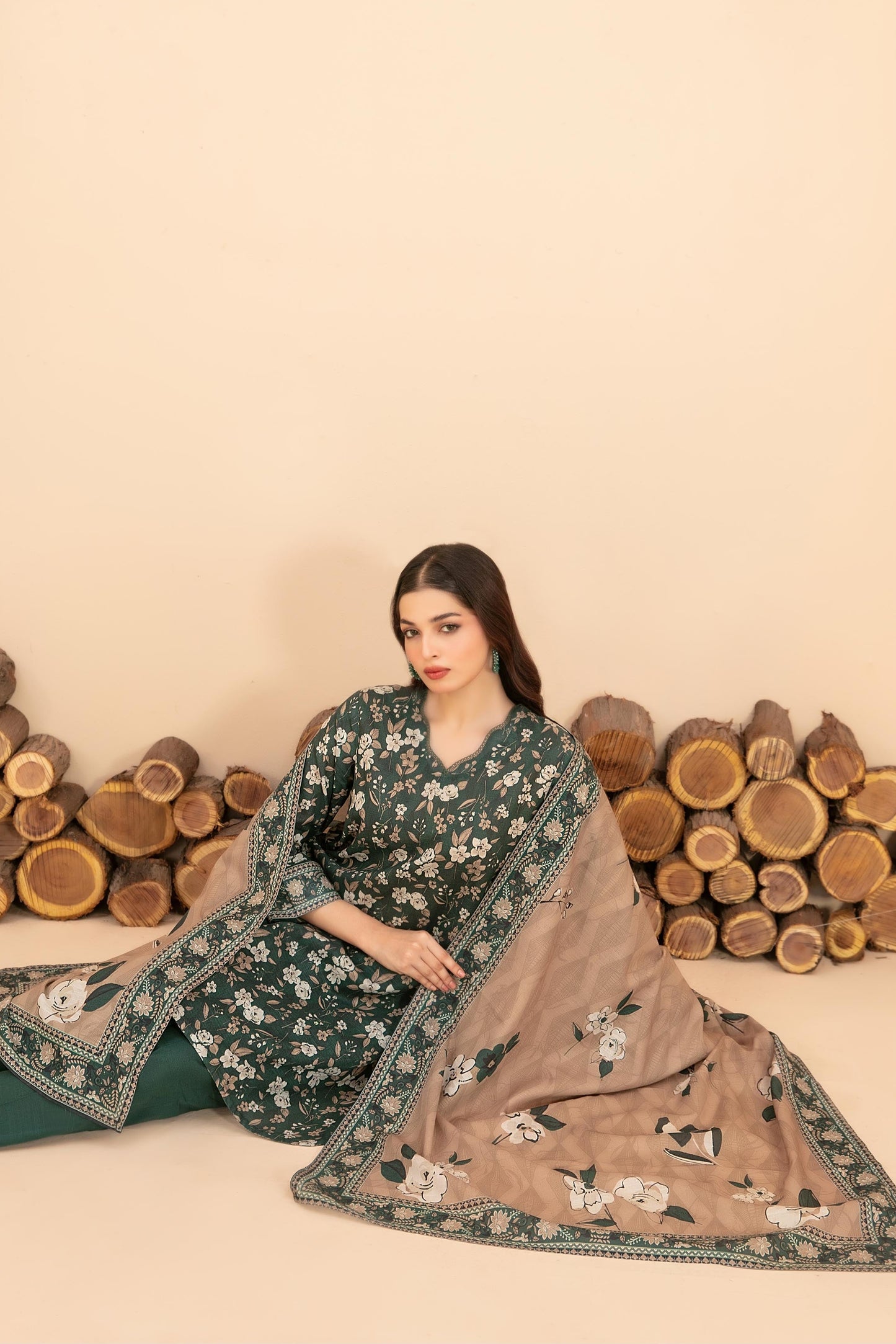 Woman in a floral outfit with a matching dupatta against a beige background with wooden logs.