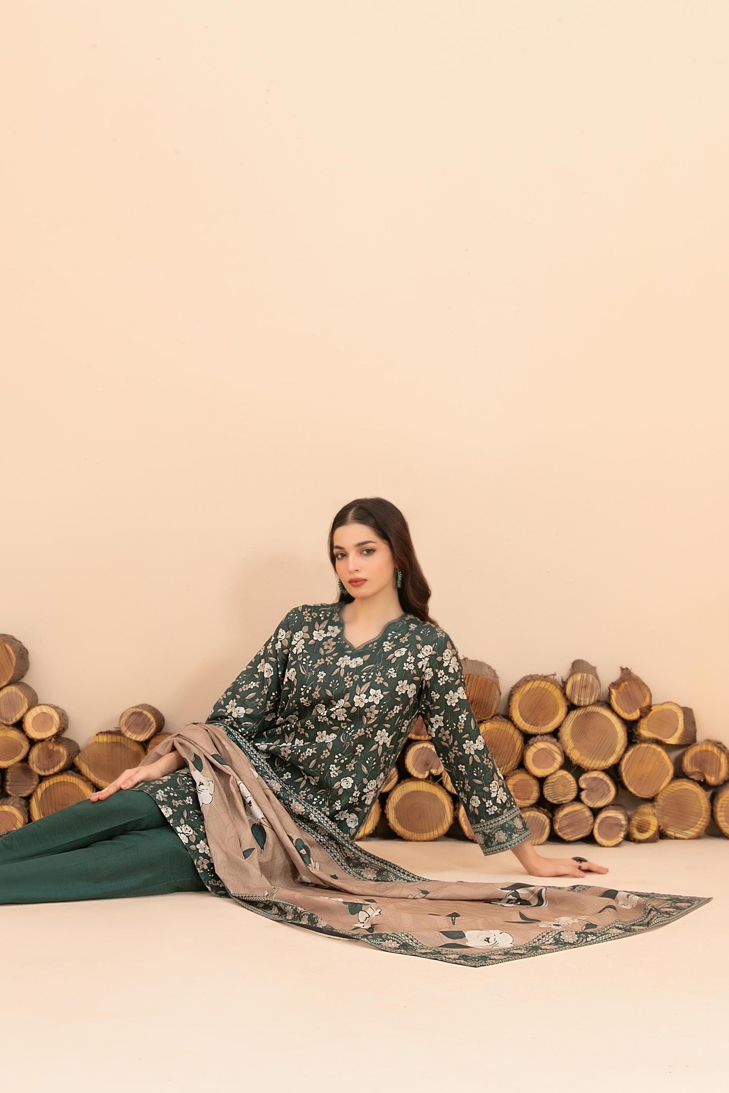 Woman in floral dress with matching dupatta sitting against a beige background with wooden logs.