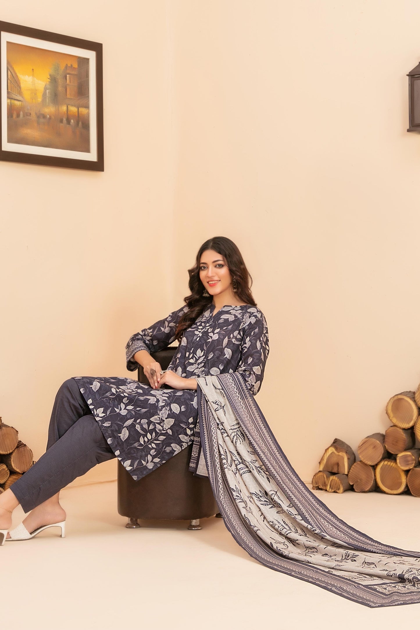 Woman sitting on a stool with a long black and white scarf in a room with wooden logs and a painting.