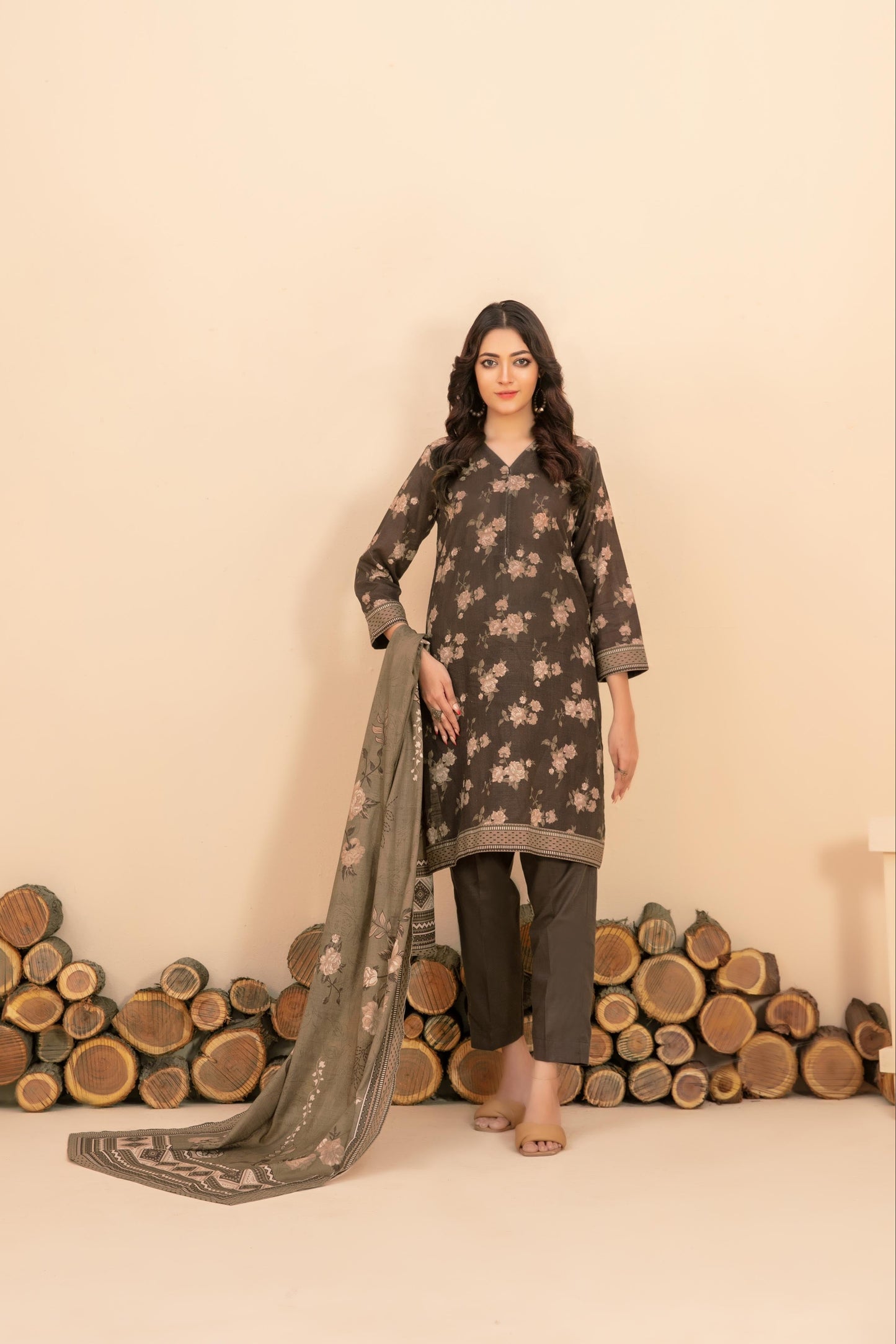 Woman in a traditional outfit with a patterned dupatta against a beige background with wooden logs.