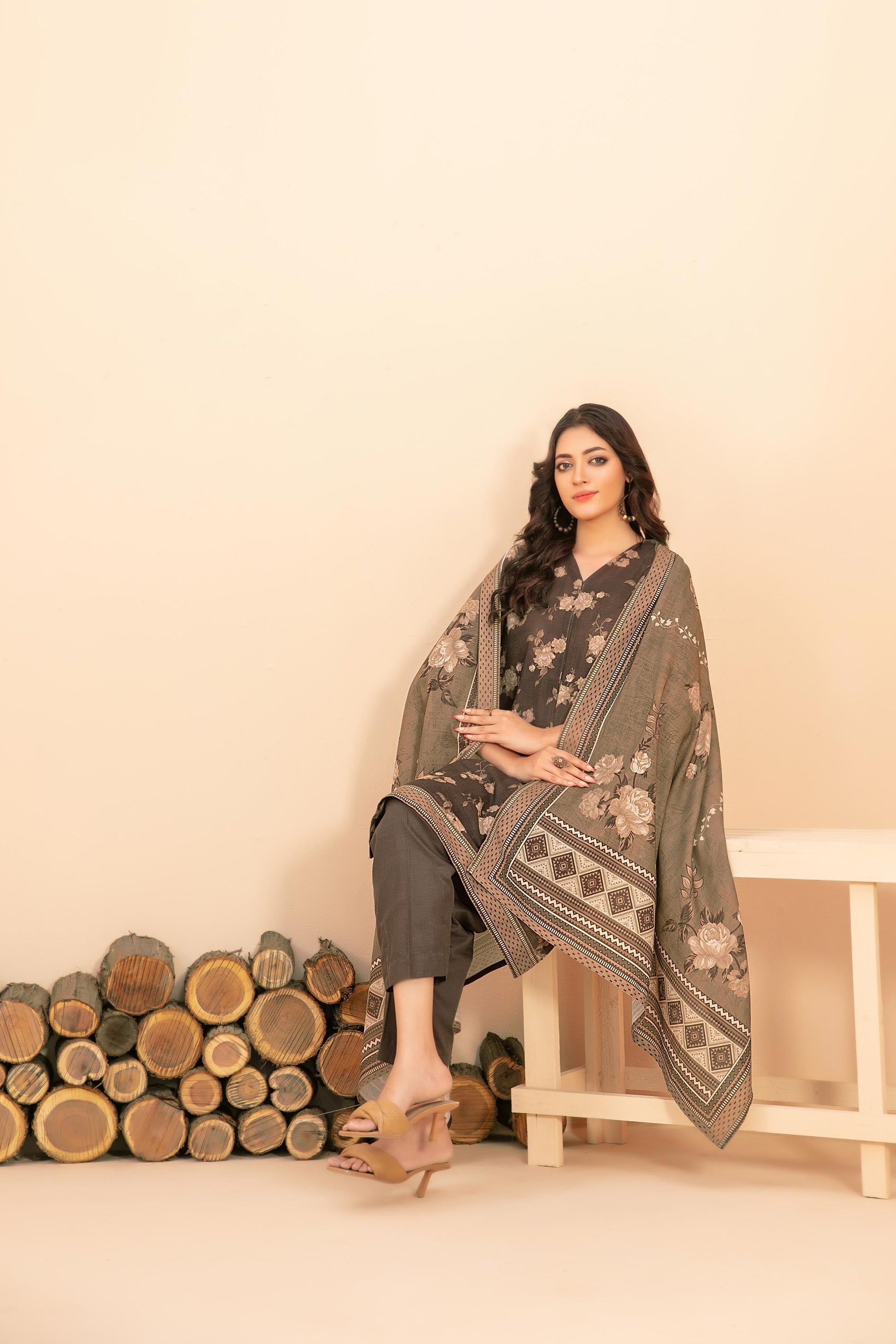 Woman in a traditional outfit with a patterned dupatta against a beige background with wooden logs.