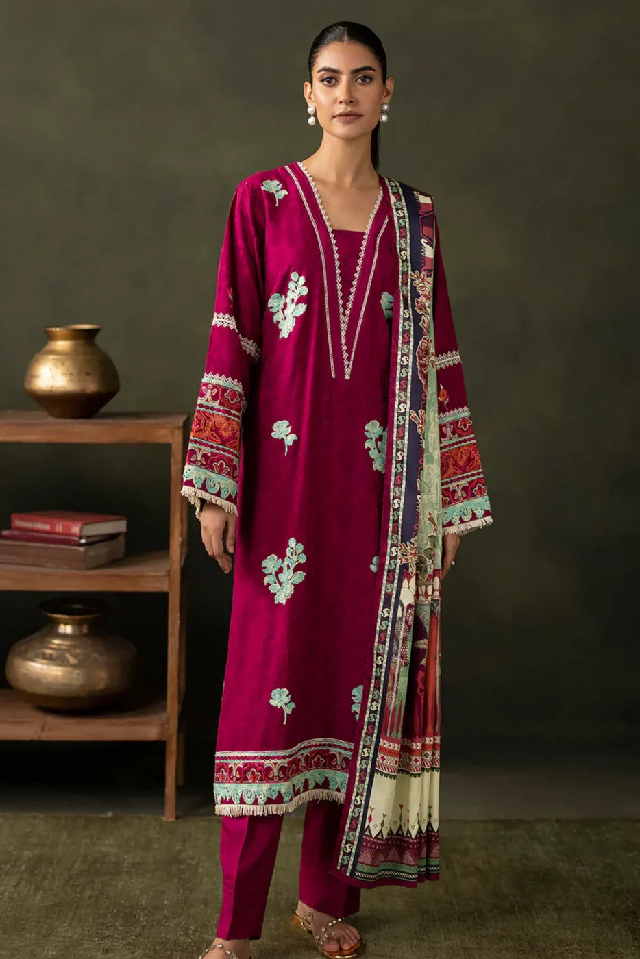 Woman wearing a magenta embroidered outfit with a matching dupatta against a dark background.