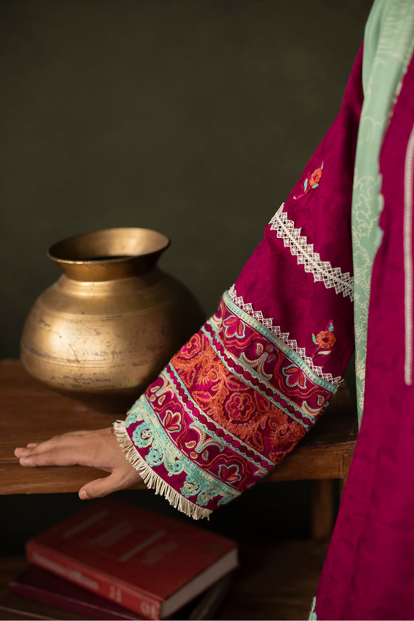 Person wearing a colorful embroidered garment with a brass pot and books in the background
