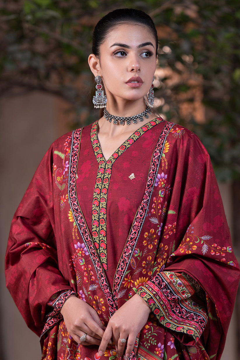Woman wearing a traditional red embroidered outfit with jewelry against a blurred natural background