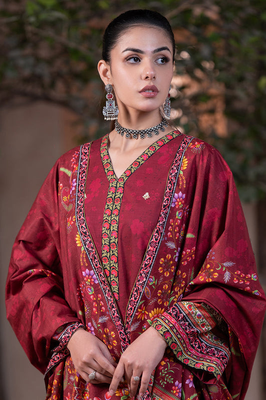 Woman wearing a traditional red embroidered outfit with jewelry against a blurred natural background
