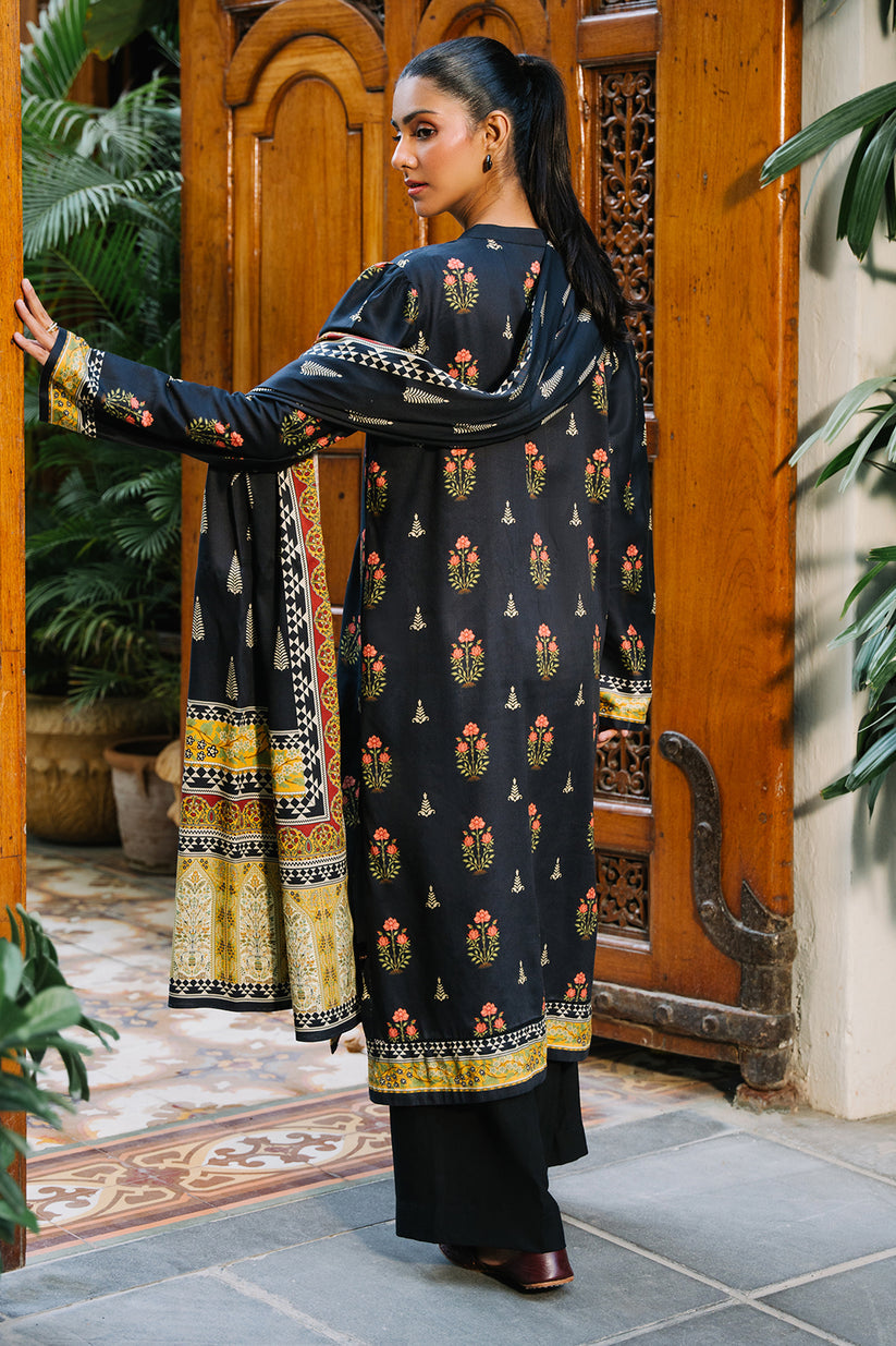 Woman in a traditional outfit standing in front of a wooden door with plants around.