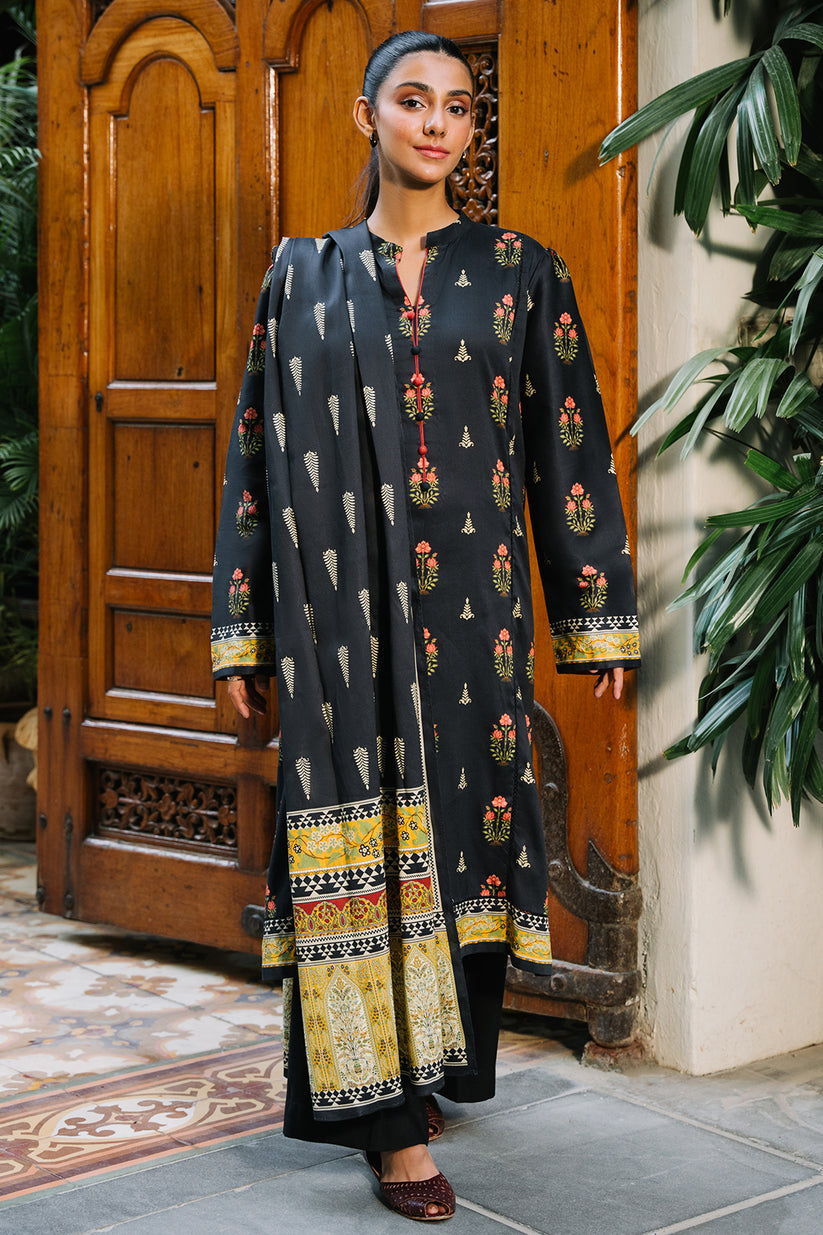Woman wearing a black traditional outfit with colorful patterns in front of a wooden door.