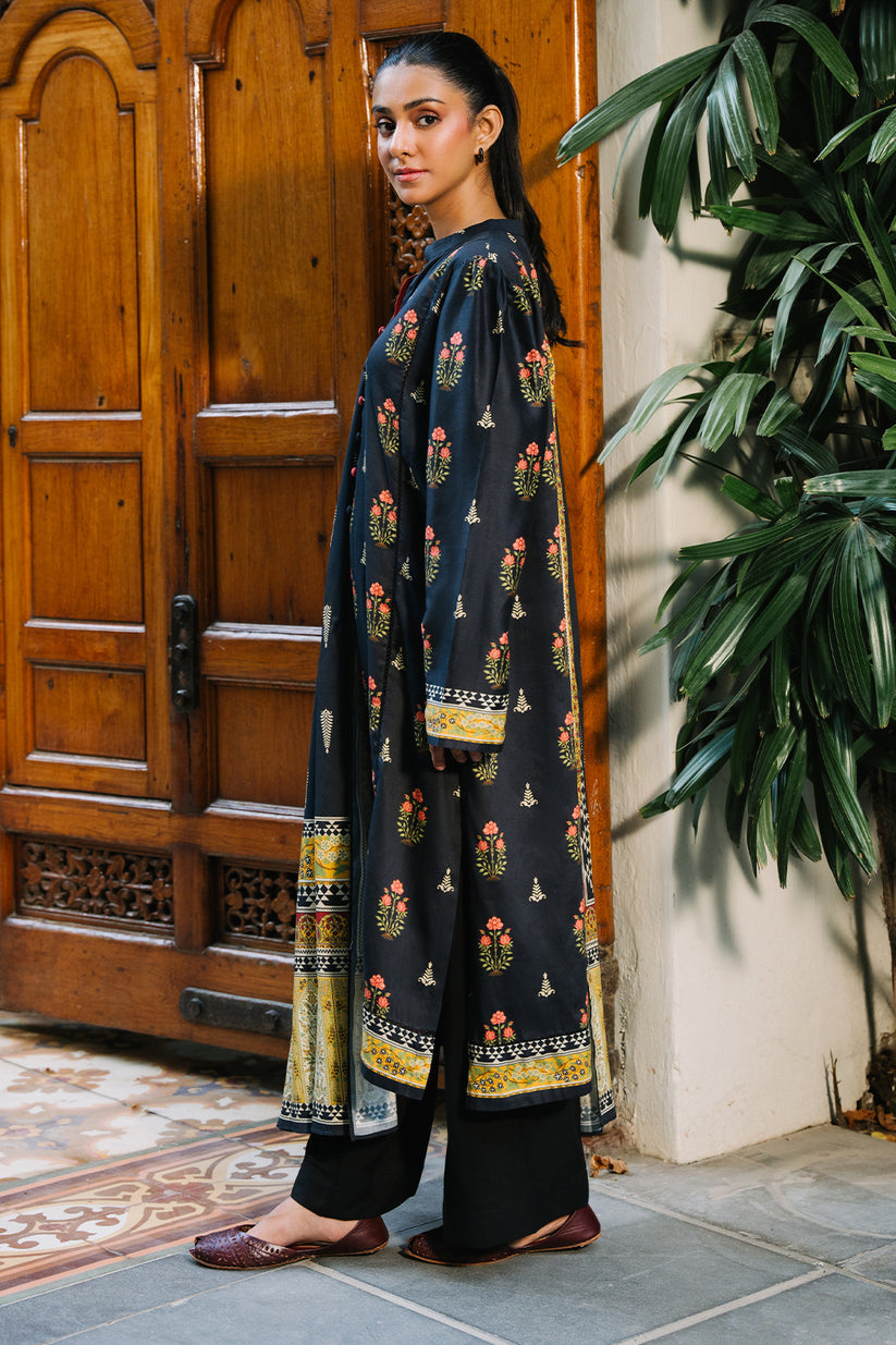 Woman in a dark blue traditional outfit with floral patterns standing in front of a wooden door.