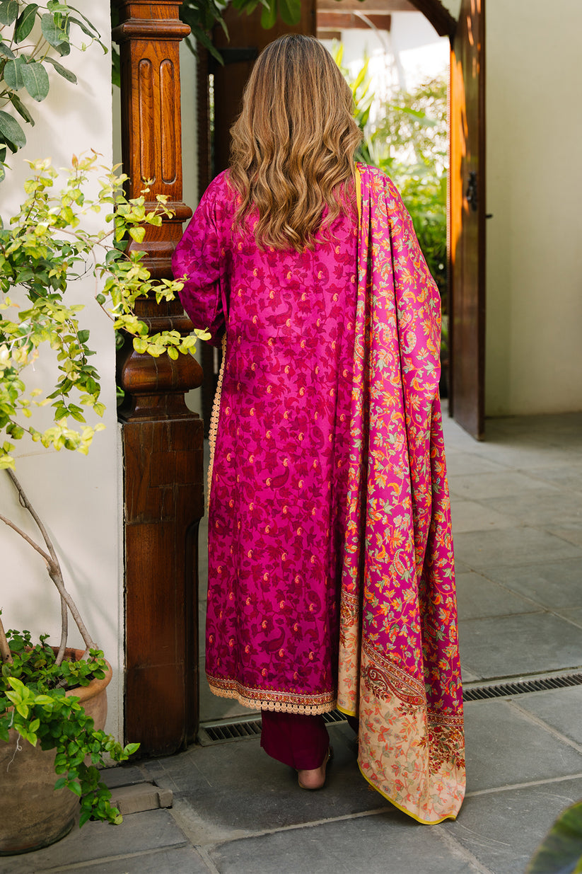 Woman in a pink traditional outfit standing in a doorway with plants around.