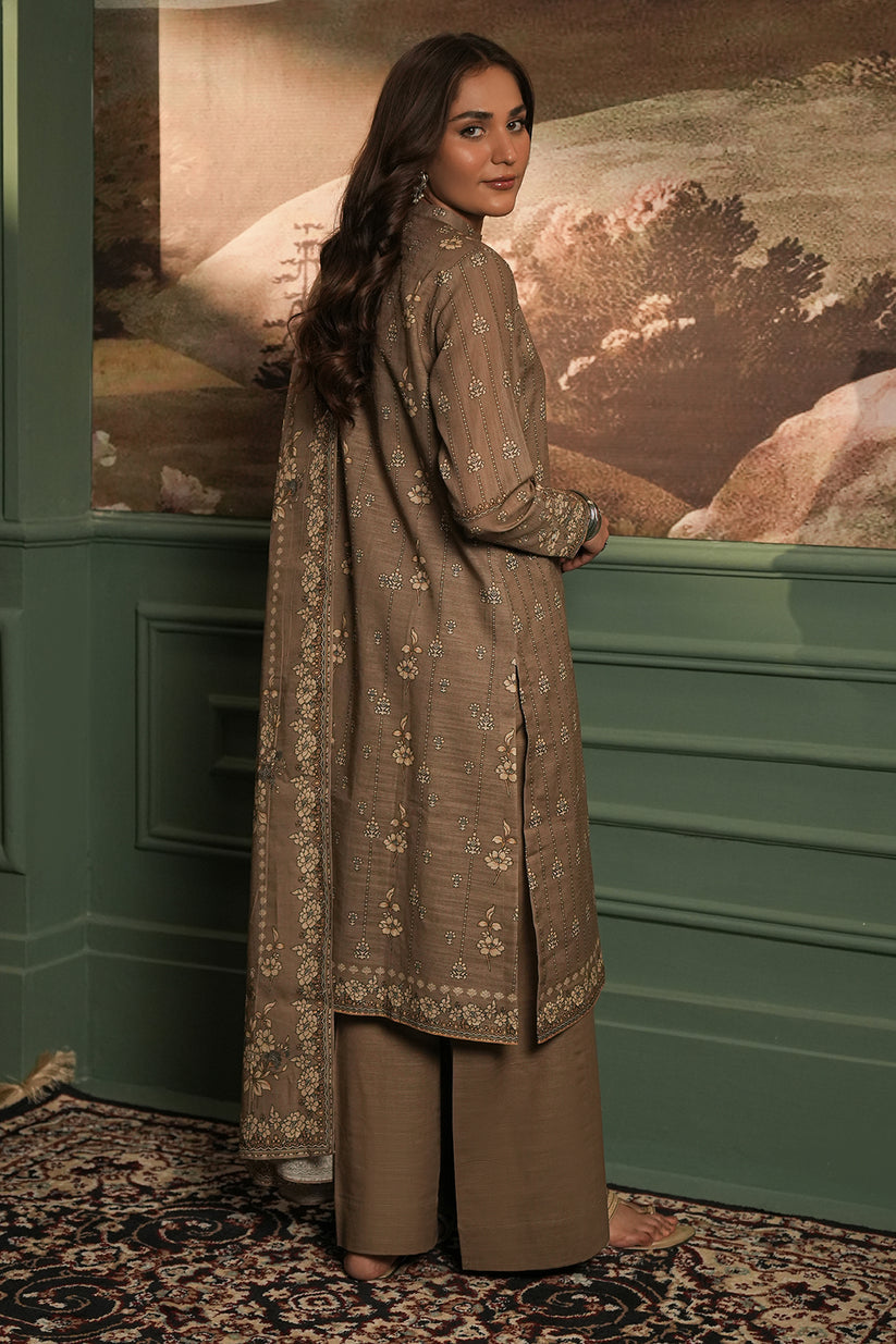 Woman in a brown traditional outfit standing in front of a decorative wall.