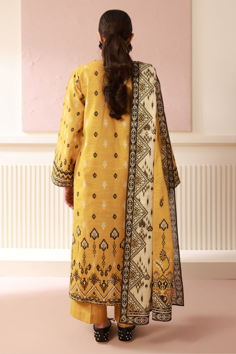 Person wearing a yellow traditional outfit with a black and white patterned scarf in a minimalistic setting.