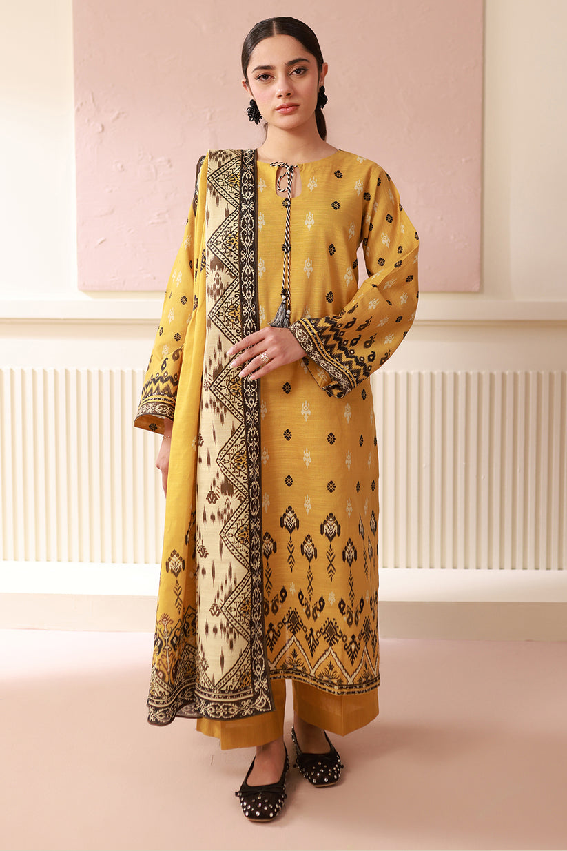 Woman wearing a yellow and black patterned traditional outfit against a pink wall.