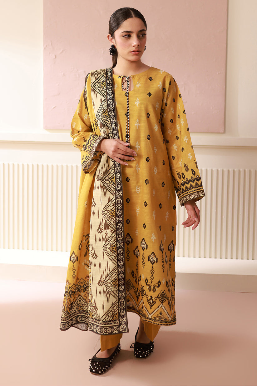 Woman wearing a yellow and black patterned outfit against a light pink wall.